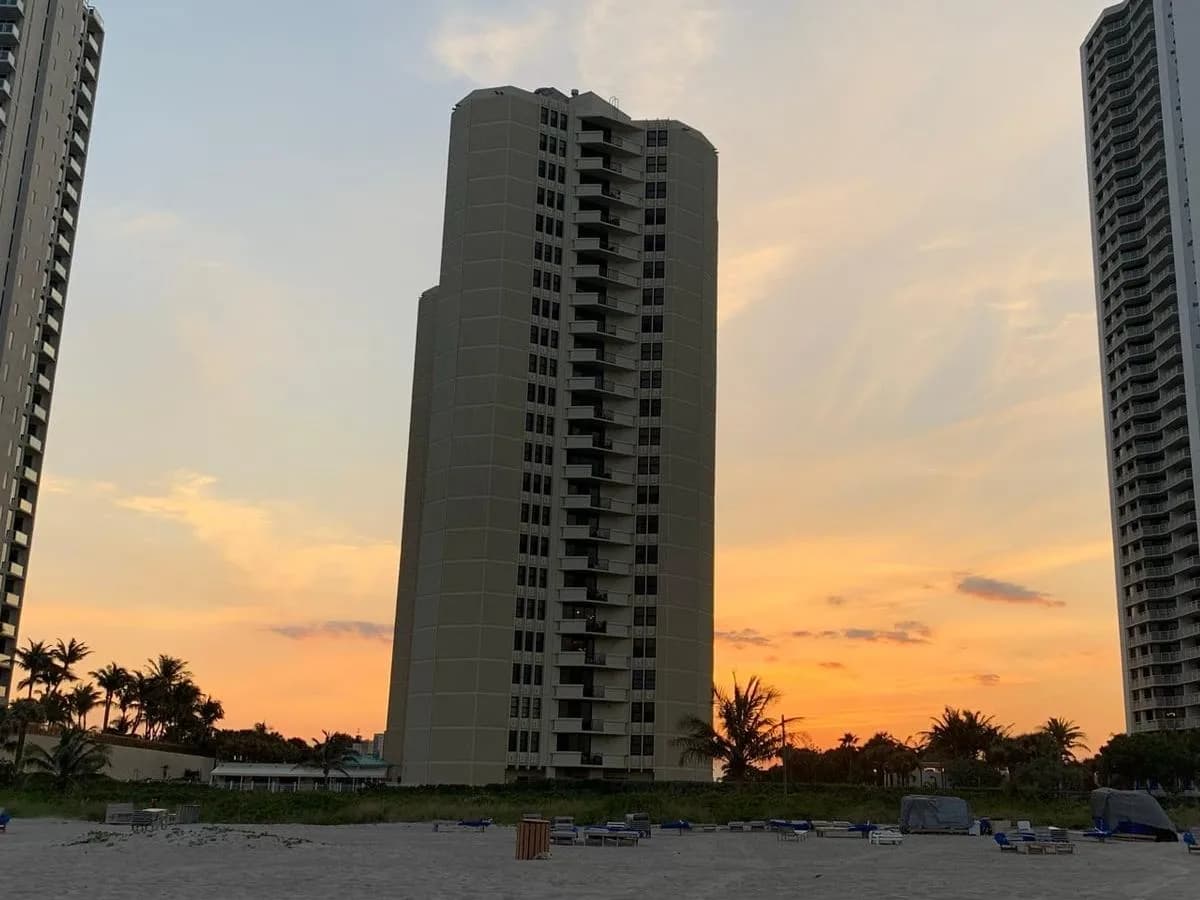 A tan Phoenix Towers building rising behind the beach and dune at sunset