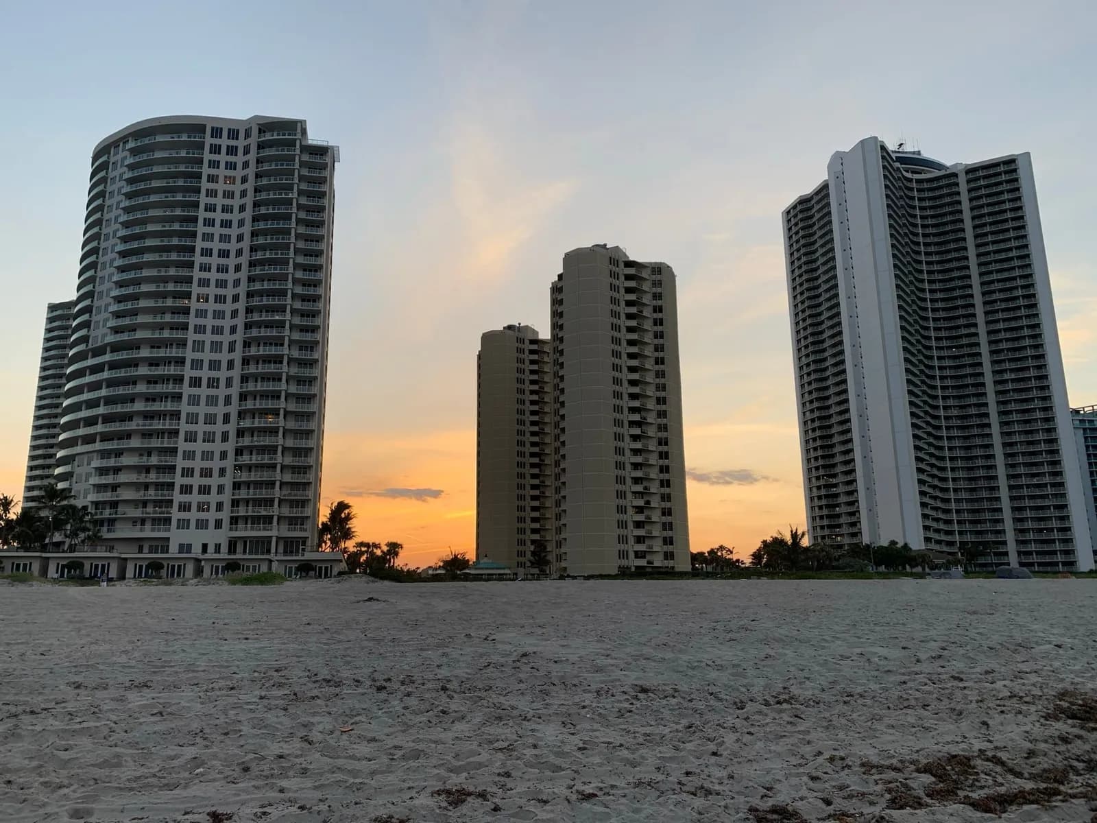 The Ritz-Carlton Singer Island, a white tower with curved balconies at left, seen from the beach at sunset