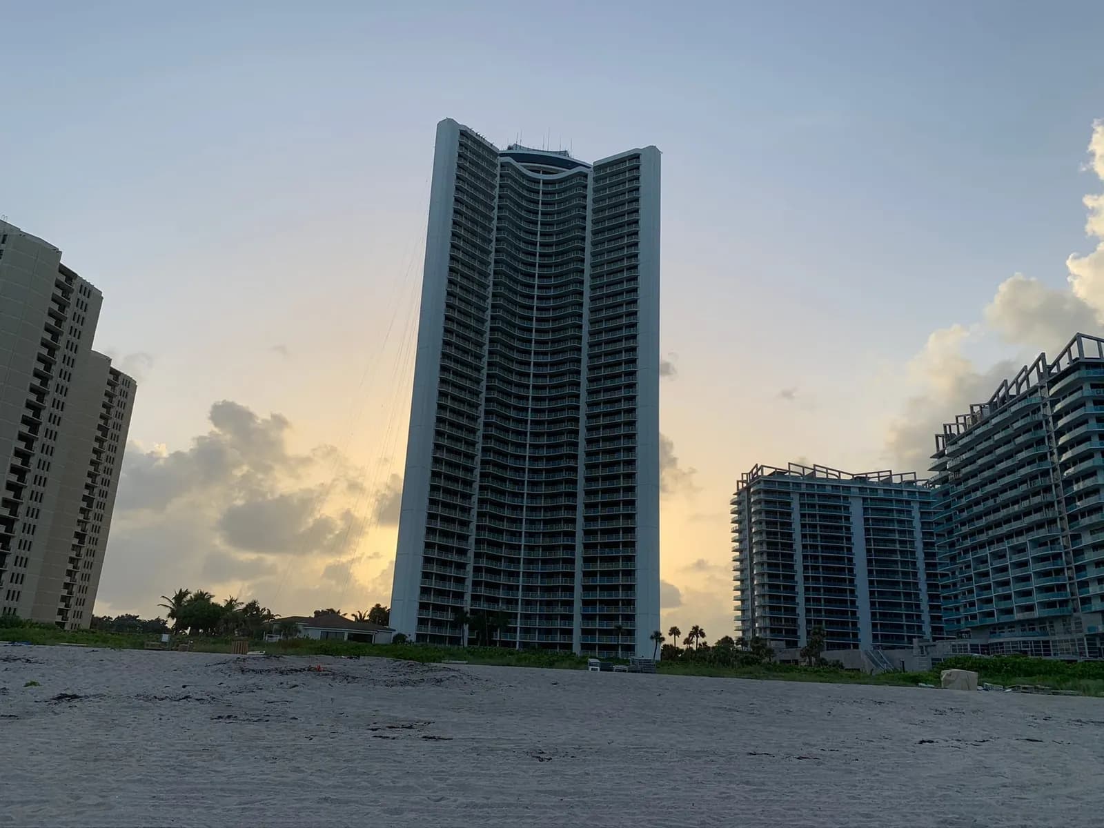 Tiara, a tall white oceanfront tower with a curved, concave front, seen from the beach at dusk